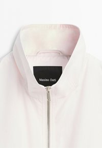 White zip-up jacket with standing collar, visible silver zipper, and black label with white "Massimo Dutti" text inside collar.
