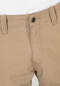 Beige Hosen aus einem strukturierten Stoff, mit einem Knopfverschluss, Gürtelschlaufen und dezenten Stickdetails.