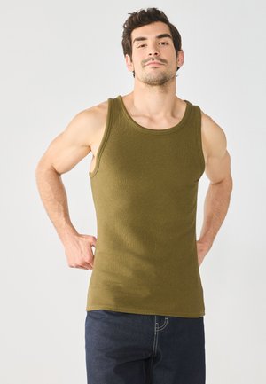 Top in cotone a costine verde oliva, con scollatura rotonda e ampie aperture per le braccia, indossato con jeans in denim scuro.