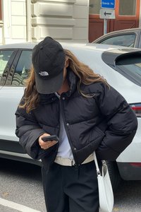 Melna pūkaina jaka ar kvadrātveida dizainu, lieliem iešūtiem apgabaliem un augstu apkakli. Uzvilkta kopā ar baltu kreklu un tumšām biksēm; rokās tur telefona ierīci.