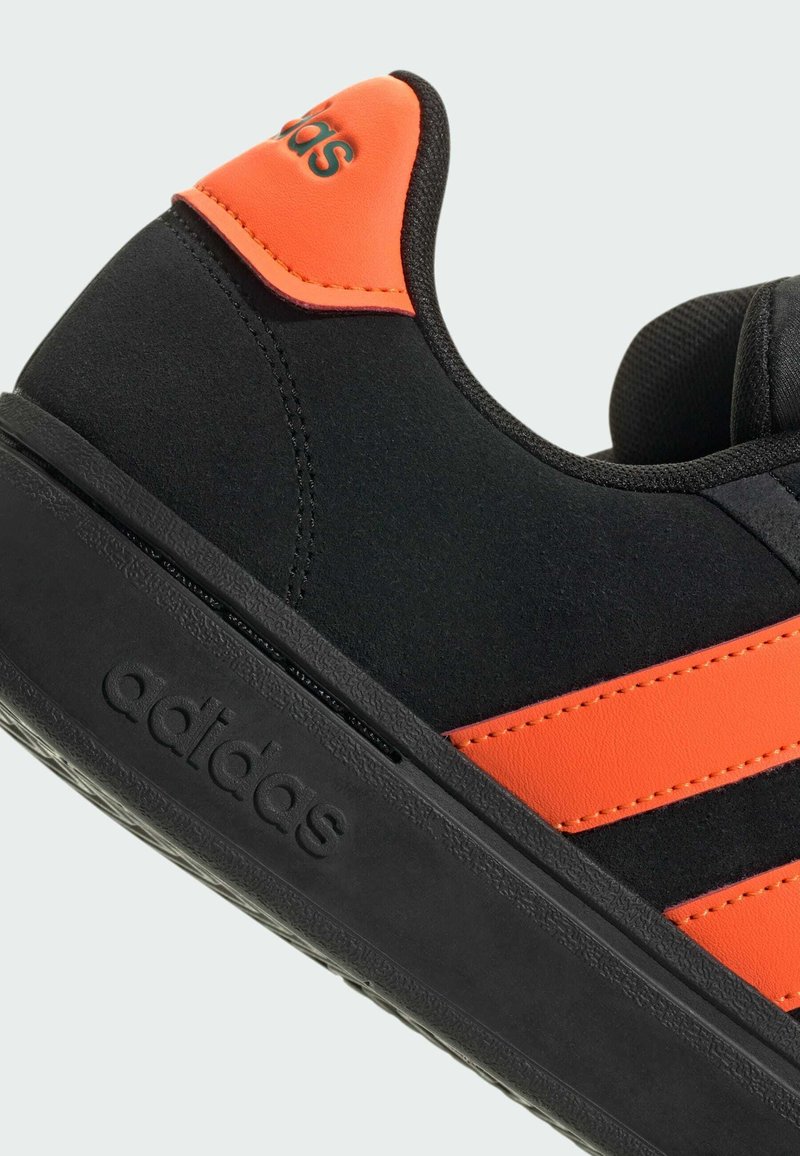 Baskets noires avec des accents oranges, dotées d'une tige en synthétique, de trois rayures texturées et d'une semelle en caoutchouc avec un logo de marque en relief.