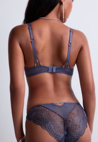 Soutien-gorge en dentelle bleu marine et culottes transparentes assorties avec une broderie complexe. Bretelles réglables et accents en matériel décoratif. Texture lisse.