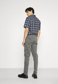 Chemise à manches courtes à carreaux bleus et verts, associée à un pantalon gris. La chemise a un col pointu ; le pantalon est droit avec une poche arrière.