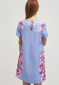 Robe bleue courte en lin, dotée de manches courtes et d'un détail en forme de trou de serrure à l'arrière. Décorée de grands motifs floraux colorés.