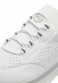 Basket de sport blanche avec un dessus en maille texturée, présentant des lacets élastiques, des accents grisés et un logo sur la languette. Design de semelle lisse.