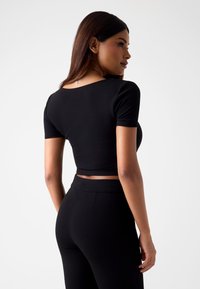 Czarny krótki top z krótkimi rękawami, o gładkiej teksturze i zaokrąglonym dekolcie. W połączeniu z czarnymi spodniami o wysokim stanie, również o gładkiej teksturze.