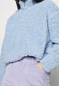Ljusblå plysch fleece zip-up topp med hög krage, med en cropped design och texturerad tyg. Matchas med lila corduroy byxor.
