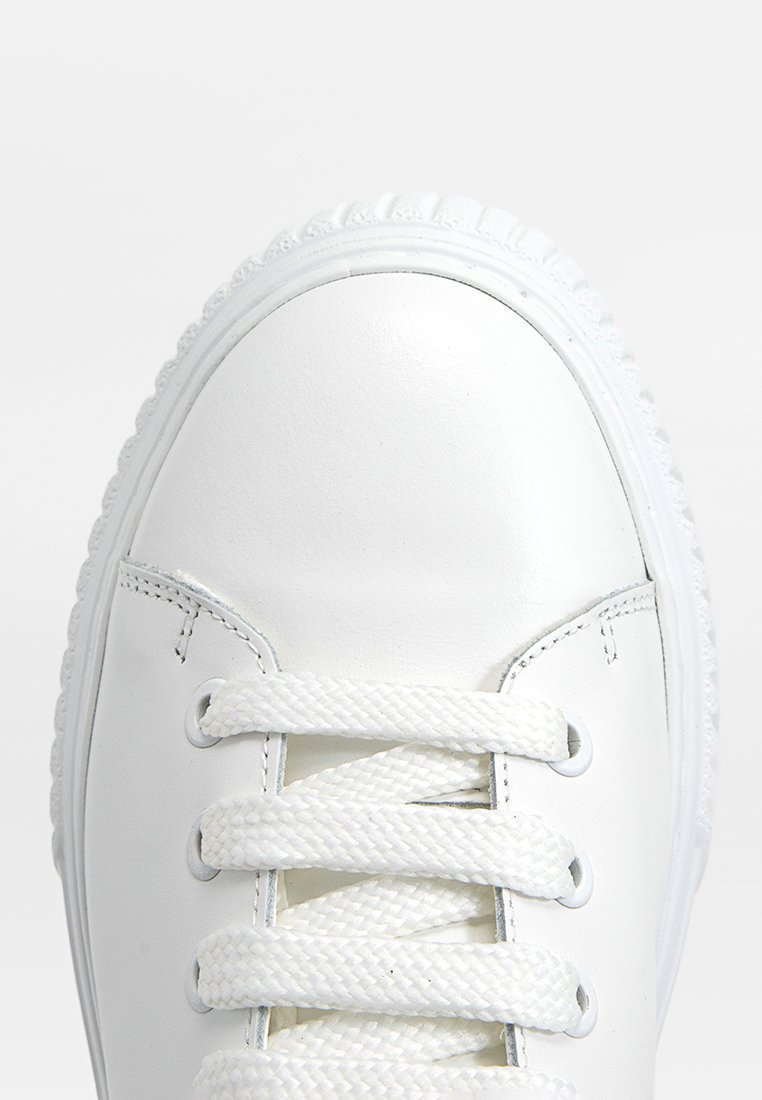 Weißes Leder-Sneaker mit runder Zehenpartie, strukturiertem Gummisohle, flachen Schnürsenkeln und minimaler Nahtdetails am Obermaterial.