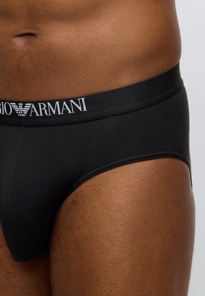 Mustat puuvillaiset alushousut, joissa on leveä elastinen vyötärönauha, jossa valkoinen "Armani"-brändäys. Sileä pinta ja vartalonmyötäinen malli.