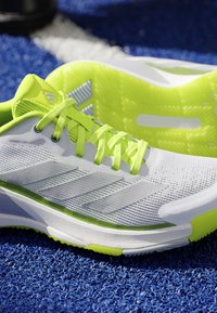 White and neon yellow athletic shoes with laces on a blue textured sports surface.