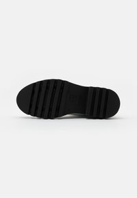 Suela de zapato de goma negra con ranuras horizontales y forma redondeada. Presenta un logotipo en relieve y marcas de tamaño. Textura suave y diseño duradero.