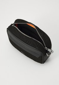 Borsa in tessuto nero a trama con chiusura a zip, interno arancione e un accento in pelle nera liscia. Presenta un logo impressa.