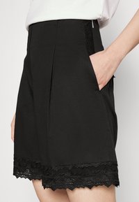 Schwarze Shorts mit einem strukturierten Spitzenbesatz am Saum und seitlichen Taschen, im maßgeschneiderten Design und mit glattem Stofffinish.