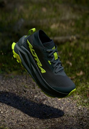 Svart trail løpesko med gule detaljer, mesh-overdel og teksturert såle. Har en pull-tab og lett design. Vibram-logo synlig.