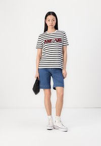 T-shirt às riscas preto e branco com "AM♥UR" em vermelho, combinada com calções de ganga azuis e ténis brancos de cano alto; segurando uma bolsa preta.