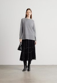 Γκρι πουλόβερ πλεχτό με άνετη εφαρμογή, συνδυασμένο με μαύρη φούστα από τούλι διακοσμημένη με παγιέτες, μαύρες μπότες μέχρι το γόνατο και μικρή μαύρη τσάντα.