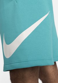 Pantalones cortos Nike color turquesa hechos de una tela suave, con un gran logo de swoosh blanco en el costado. El diseño incluye detalles de dobladillo cosido.
