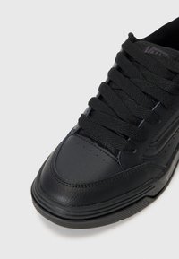 Black leather sneaker with textured upper, flat laces, padded collar, and rubber sole. Perforations on the toe for breathability.