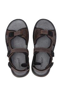 Braune verstellbare Sandalen mit zwei Klettverschlüssen, einem strukturierten Fußbett und einer schwarzen Sohle. Logo auf dem Fußbett sichtbar.
