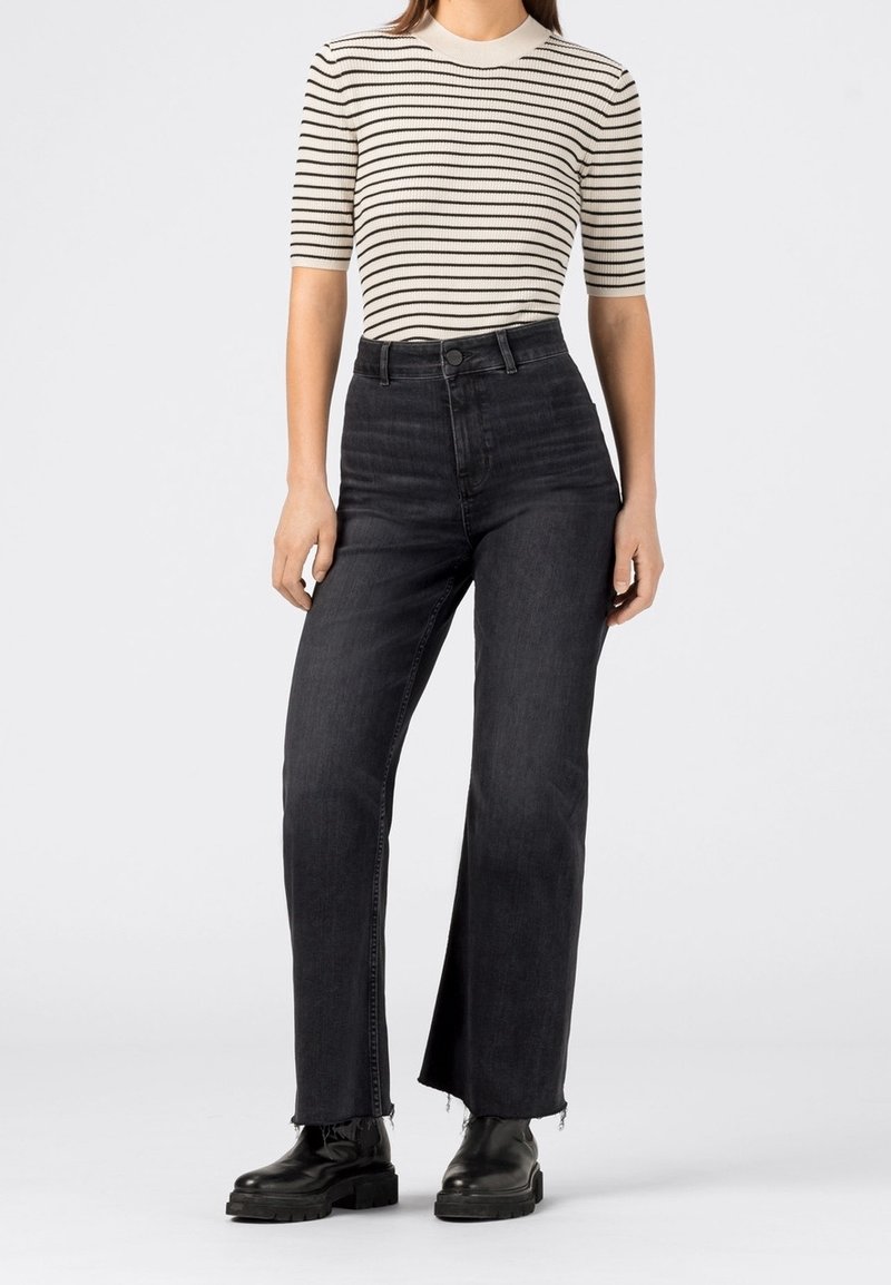 Hochtaillierte schwarze Jeans mit geradem Bein, fransigen Säumen und einem klassischen Knopfverschluss, kombiniert mit einem gestreiften Kurzarmoberteil.