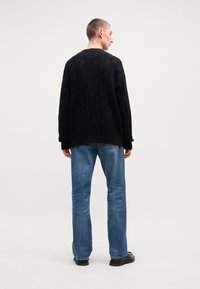 Musta kyntöpuuvillaneule, jossa on geometrinen kuvio, päälläsiniset farkut. Asusteena mustat kengät.