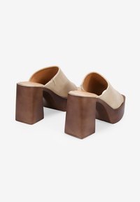 Zapatos de plataforma beige con un acabado suave y parte trasera abierta, que presentan un tacón grueso y cuadrado de color marrón y mínimos acentos de costura.