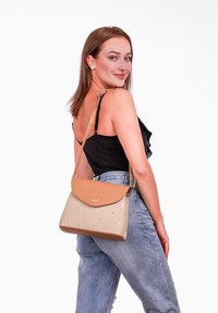 Beige ramenní taška s hnědou klopou, zdobená roztroušenými puntíky. Vyrobena z texturovaného materiálu, s nastavitelným popruhem.