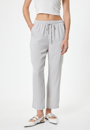 Light gray, loose-fitting trousers made from soft fabric. Features an elastic waistband with drawstring and side pockets. Paired with white shoes.