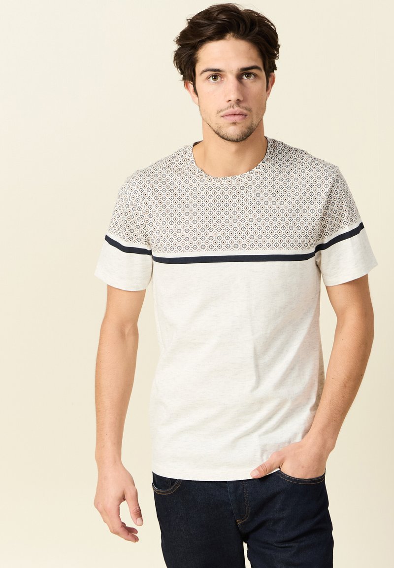 Camiseta de manga corta en gris claro con una sección superior estampada que presenta formas geométricas; franja oscura sólida a través del pecho.