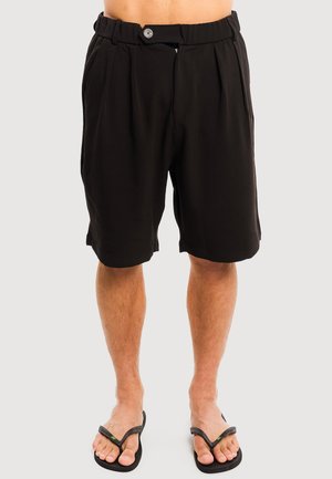 Czarne męskie szorty do kolan z guzikiem i elastycznym pasem, noszone z czarnymi klapkami, pokazane od talii do stóp.