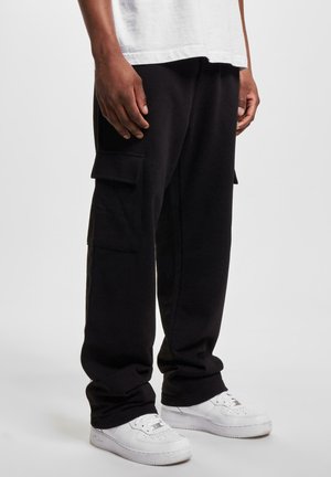 Schwarze Cargo-Hosen aus weichem Material, mit zwei Seitentaschen, lockerer Passform und elastischen Bündchen, kombiniert mit weißen Sneakers.