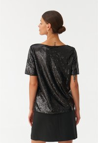 T-shirt nera con paillettes, dalla vestibilità ampia, maniche corte e scollatura rotonda. Il retro presenta uno stile drappeggiato e una texture liscia.