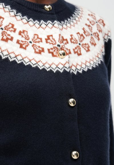 Cárdigan azul marino con un patrón en blanco y naranja en la parte superior. Cuenta con botones dorados, punto texturizado y un corte relajado diseñado para la comodidad.