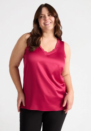Blusa senza maniche fucsia con scollatura a V e bordo ondulato, realizzata in tessuto morbido e liscio, abbinata a pantaloni neri.