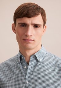 Koszula zapinana na guziki w jasnoniebieskim kolorze z geometrycznym wzorem w ciemniejszym odcieniu niebieskiego. Posiada rozkładany kołnierzyk i białe guziki.