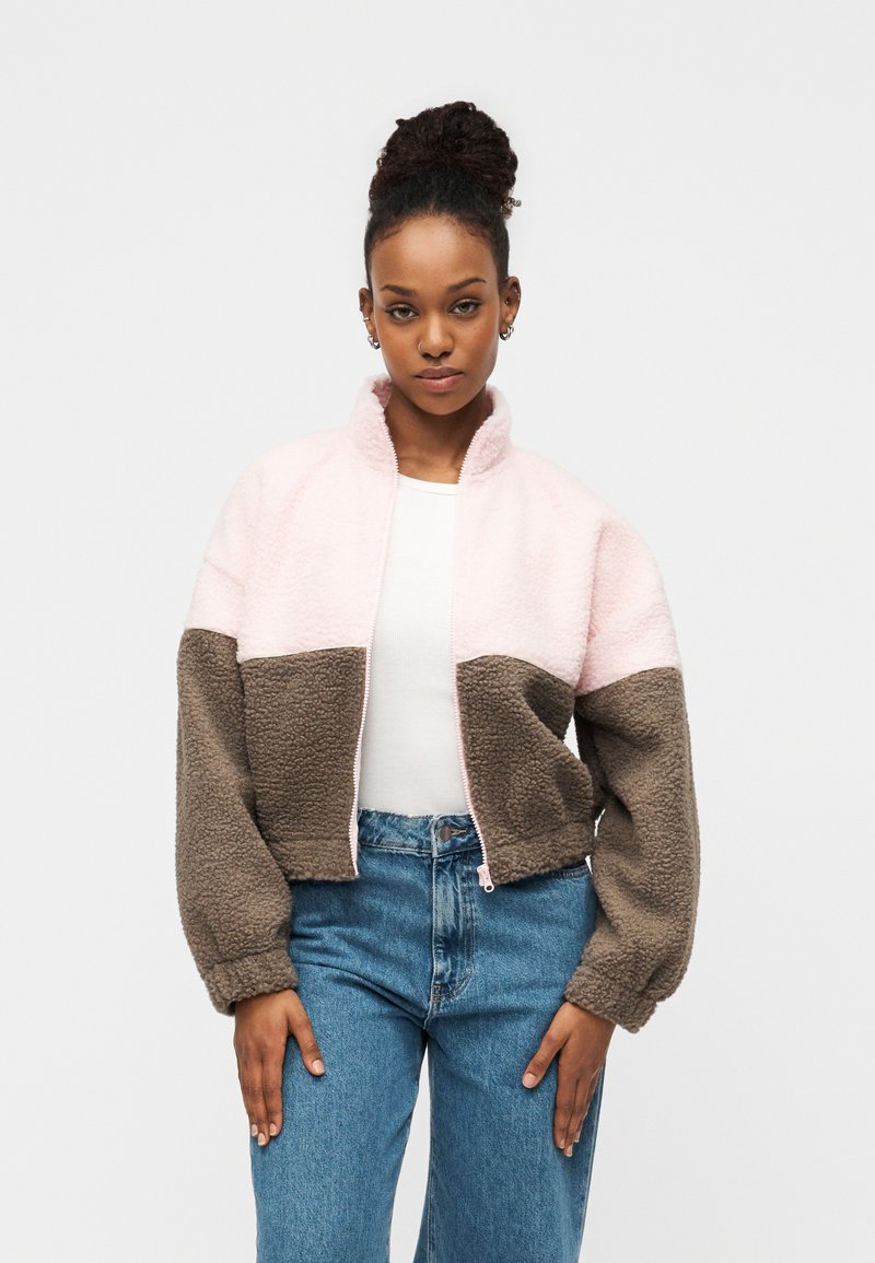Ζακέτα φλις με κοντό σχεδιασμό, που διαθέτει ροζ πάνω και καφέ κάτω πάνελ, ψηλό γιακά και κλείσιμο με φερμουάρ. Μαλακή, υφή με υφή.