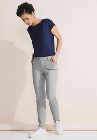 Top de manga corta azul marino combinado con pantalones ajustados gris claro con bolsillos laterales, luciendo zapatillas blancas sobre un fondo neutro.