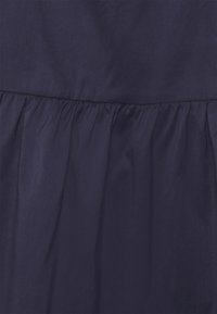 Tecido azul-marinho escuro com uma textura suave, apresentando um design franzido na bainha para adicionar volume. Superfície lisa e uniforme.