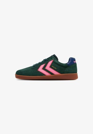 Zapatilla de ante verde oscuro con rayas rosa en forma de chevron, suela marrón y lengüeta azul en el talón con marca rosa, vista de lado.
