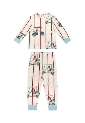 Kind mit lockigem Haar, das barfuß auf einem weißen, strukturierten Stuhl steht und einen Schlafanzug mit Golfwagen und braunen Hunden auf weißem Hintergrund mit roten Streifen trägt.