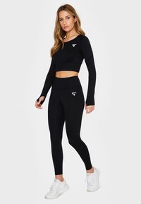 Black long-sleeve crop top and high-waisted leggings made of stretchy fabric, featuring a white logo on the chest and side pocket.