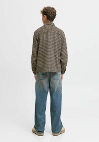 Camicia a quadri marrone e crema con colletto, abbinata a jeans larghi e sbiaditi blu e calzature beige.