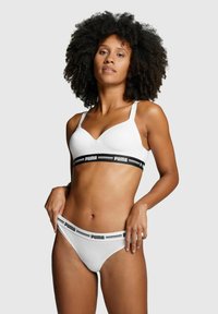 Weißes Bralette mit verstellbaren Trägern, versehen mit einem schwarzen Band mit "PUMA"-Logo. Passender weißer String mit schwarzem Logo-Band. Glatte Textur.