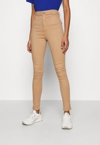 Tan högmidjade skinny jeans med knappstängning fram och fickor, kombinerat med vita sneakers. Slät tyg, åtsittande design.