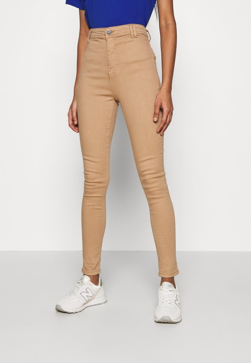 Tan högmidjade skinny jeans med knappstängning fram och fickor, kombinerat med vita sneakers. Slät tyg, åtsittande design.