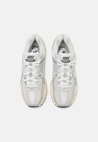 Nike Vomero 5 sneakers i ljusgrått med mesh-material, texturerade detaljer, vita snören, svart sula och framträdande logotyp på tungan.