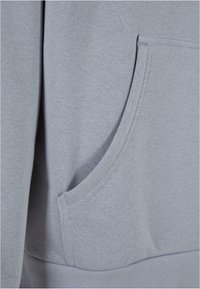 Sudadera de color gris claro con un bolsillo tipo canguro. Textura suave, costuras cosidas y ajuste relajado en el dobladillo y los puños.
