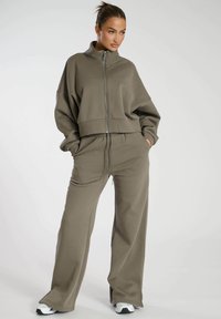 Olijfgroene cropped zip-up sweatshirt met hoge kraag, gecombineerd met wijde broekspijpen. Glad materiaal met een relaxte pasvorm.