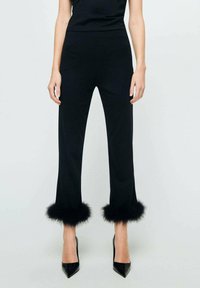 Pantalons ajustés noirs avec une coupe droite, ornés d'une bordure en fourrure noire aux poignets et associés à des talons aiguilles noirs.