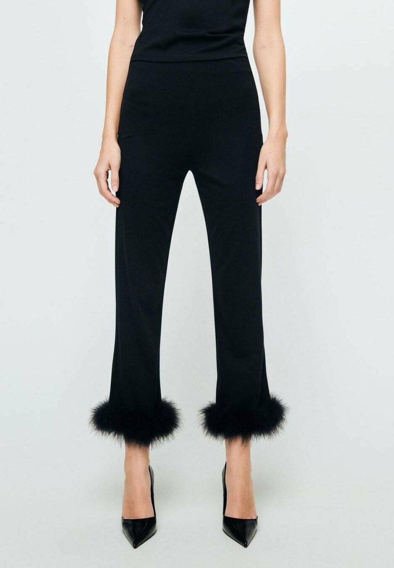 Pantalons ajustés noirs avec une coupe droite, ornés d'une bordure en fourrure noire aux poignets et associés à des talons aiguilles noirs.